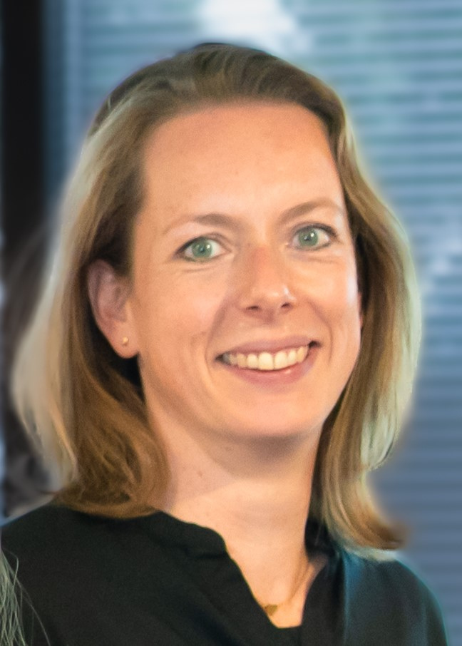 Re-integratiecoach Tineke Driessen lachend voor de camera, met op de achtergrond een raam met raamdecoratie.
